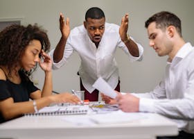 Three colleagues in a heated argument at the office, highlighting workplace stress.